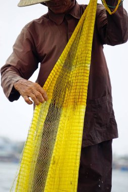 Vietnamlı balıkçı küçük bir teknede balık ağıyla balık tutuyor.