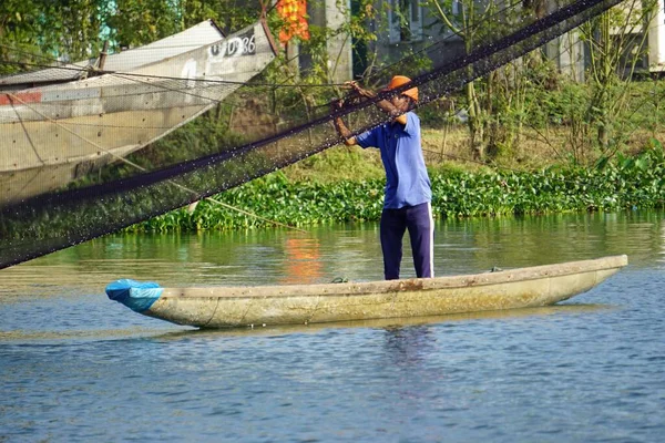 Ein Fischer wirft sein Netz aus einem traditionellen Boot am