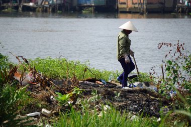 ho chi minh city, Vietnam, Şubat 2020: Nehir kıyısında atık yakan kadın