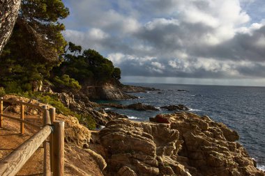 Bulutlu gökyüzü ile kayalık kıyı arasında yol