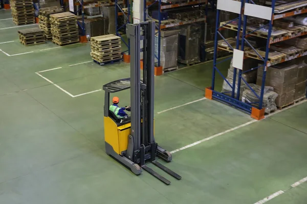 Depoda çalışan sarı forklift mallarla dolu rafların arasında.