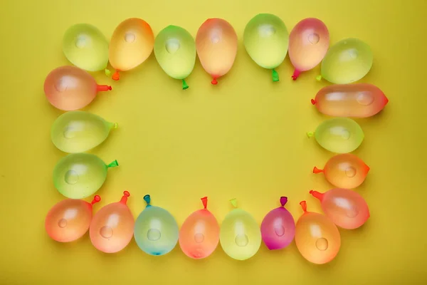 border of multicolored water balloons, flat lay with yellow copy space