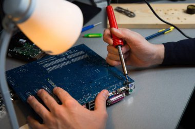 Elektrikçi elleri atölyede lehimleme demiriyle çalışıyor.