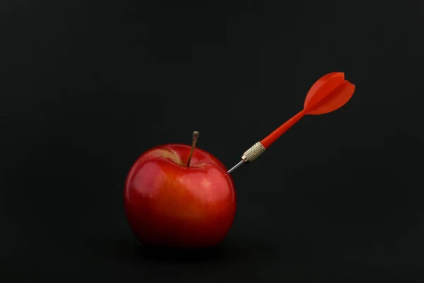 dart sticks out of an apple on a black background. dart hit an apple on a black background