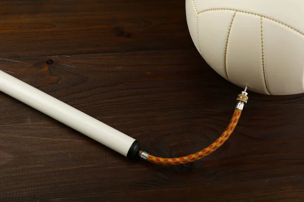 Tahta arka planda iğne ve voleybol topu olan bir pompa. Topu şişiriyorum.