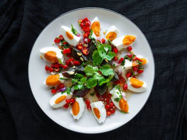 Tuzlu yumurta ve Century yumurta salatası Tayland yemeği menüsü, baharatlı, ekşi, tuzlu, tatlı. Ana malzemeler, tuzlu yumurta ve yüzyıllık yumurta. Beyaz tabakta soğan, kişniş, kireç, biber, soğan. Siyah arkaplan.