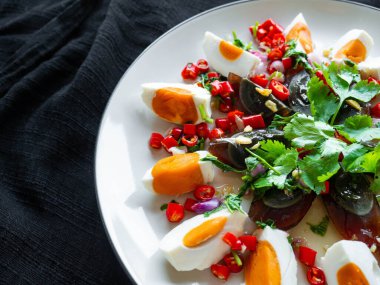 Tuzlu yumurta ve Century yumurta salatası Tayland yemeği menüsü, baharatlı, ekşi, tuzlu, tatlı. Ana malzemeler, tuzlu yumurta ve yüzyıllık yumurta. Beyaz tabakta soğan, kişniş, kireç, biber, soğan. Siyah arkaplan.