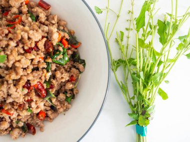 Beyaz bir tabakta doğranmış fesleğen, Tayland yemeği sıcak ve baharatlı. Malzemeler fesleğen ve sarımsak. Kıyma ve acı biber, beyaz arka plan.