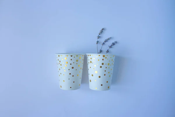 Two paper cups with golden dots and lavender on a blue background. Flat lay