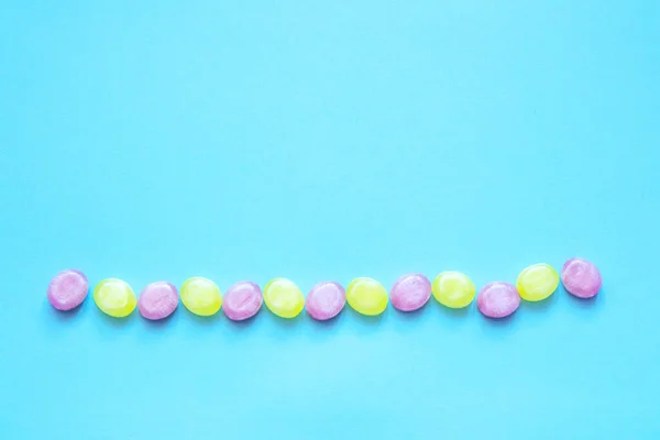 Multicolored candy laid out in line on a blue background. With copy space. Flat lay