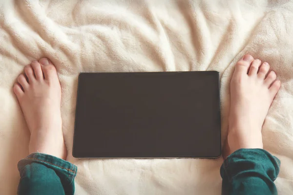 Teenager sitting on the bed and looking at tablet screen