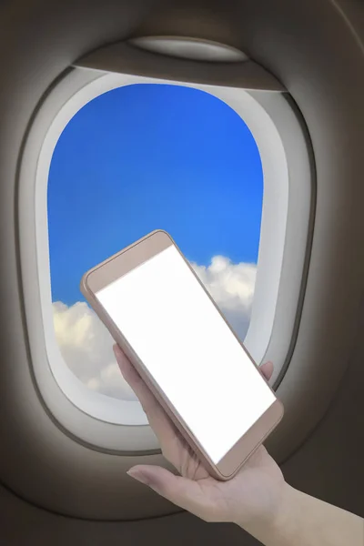 Hand holding smart phone with blank screen above cloud and blue sky from airplane window, input text idea
