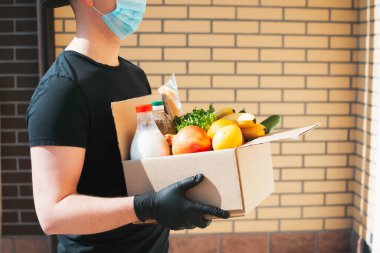 Koruyucu maskeli bir kurye ve eldivenli bir kutu farklı yemek getiriyor. Corona virüsü salgını sırasında yemek teslimatı. İyi teslimatlar. Paket yemek..