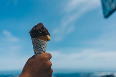 Adamın eli dondurma külahında mavi gökyüzüne karşı. 