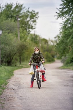 Kırmızı çizmeli bisiklet süren maskeli çocuk. Renkli bir geçmişi var. Beyaz tıbbi maske izole. Virüs koruma konsepti. Erkek çizgi film karakteri. Yaşam tarzı tasarımı için güzel bir portre.
