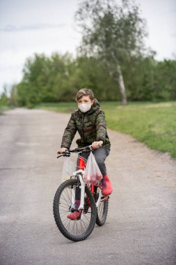 Maskeli çocuk ve kırmızı çizmeler eve elma taşıyor. Tıbbi konsept. Doğa konsepti. Virüs koruması. Sağlık kavramı.