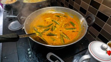 El, balığı daha lezzetli yapmak için spatula kullanarak balık kafasındaki körinin içine biraz hindistan cevizi sütü karıştırdı. Balık kafası körisi, Malezya mutfağında Hint ve Çin kökenli bir yemektir..