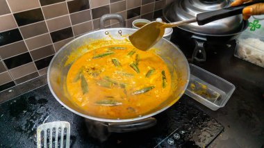 El, balığı daha lezzetli yapmak için spatula kullanarak balık kafasındaki körinin içine biraz hindistan cevizi sütü karıştırdı. Balık kafası körisi, Malezya mutfağında Hint ve Çin kökenli bir yemektir..