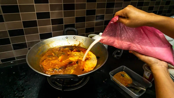 手在鱼的头上放一些椰子汁 放在金属锅里的咖哩里 使食物更好吃 鱼头咖哩是马来西亚菜中的一道菜 原产于印度和中国 — 图库照片