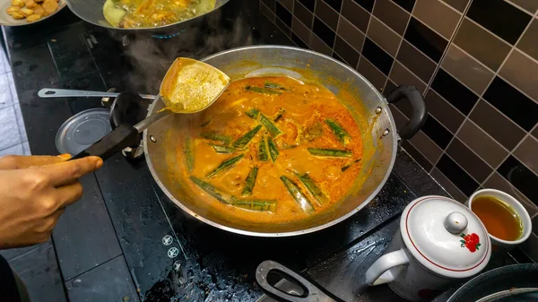 手拿些椰子汁在鱼头咖哩里加入金属锅里 用木薯把食物搅拌得更好吃 鱼头咖哩是马来西亚菜中的一道菜 原产于印度和中国 — 图库照片