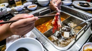Japon büfe restoranında kaynamış çorbaya dalmadan önce bir dilim çiğ eti tutan çubuğun yakın plan görüntüsü..
