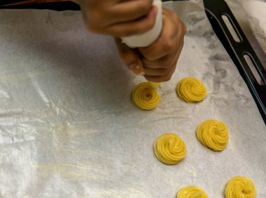 Kızın kremalı pasta topunu fırına atmadan önce bir sırada boru torbasını kullanmasını yakından izle..