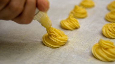 Kızın kremalı pasta topunu fırına atmadan önce bir sırada boru torbasını kullanmasını yakından izle..