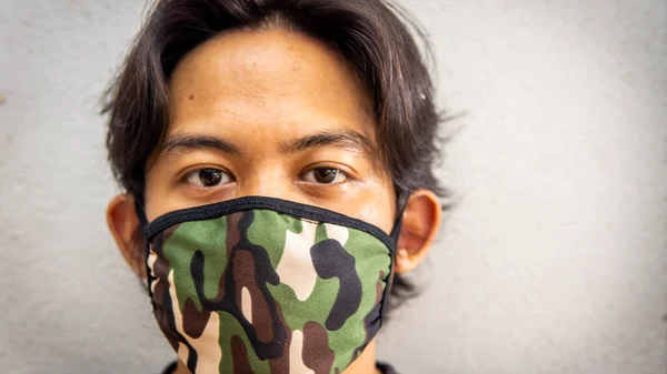A portrait of a young Malay man wearing an army camouflage face mask on isolated white background. Protection step to avoid spreading viruses and diseases.
