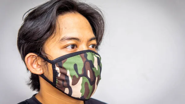 A portrait of a young Malay man wearing an army camouflage face mask on isolated white background. Protection step to avoid spreading viruses and diseases.