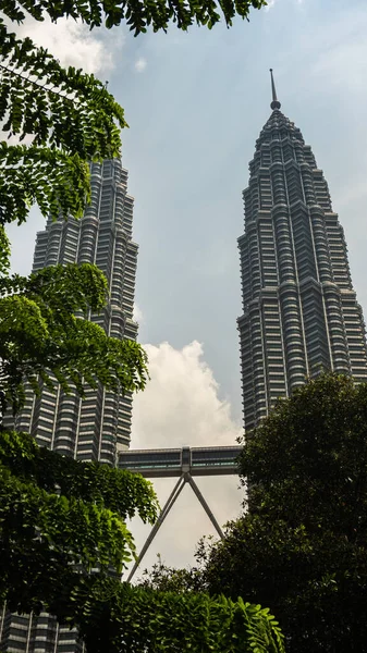 马来西亚吉隆坡 2019年7月30日 从绿树自然景观看著名的Petronas Twin Tower或Klcc 周围是高耸的摩天大楼和多云的天空 — 图库照片