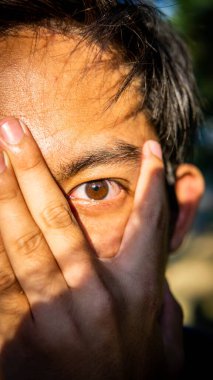 Erkek gözlerinin portresinin yakın görüntüsü parmak boşluklarından, gün doğumunun doğal ışığından ve yüzlerindeki gölgelerden görülüyor..