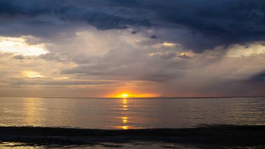 Sabah Tanjung Aru Plajı 'nda alacakaranlıkta gün batımının görüntüsü. Koyu mavi gökyüzü ve turuncu güneş deniz suyuna yansıyor..