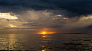 Sabah Tanjung Aru Plajı 'nda alacakaranlıkta gün batımının görüntüsü. Koyu mavi gökyüzü ve turuncu güneş deniz suyuna yansıyor..