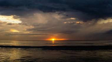 Sabah Tanjung Aru Plajı 'nda alacakaranlıkta gün batımının görüntüsü. Koyu mavi gökyüzü ve turuncu güneş deniz suyuna yansıyor..