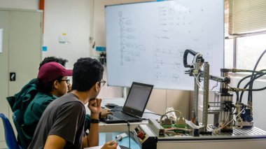 Bangi, Malezya - 2 Ekim 2019: Mühendislik öğrencileri laboratuarda dizüstü bilgisayar kullanarak otomasyon sisteminde verilen görevi tartışıyor ve çözüyorlar. Resim gürültü azaltma içeriyor.