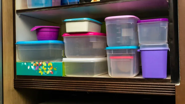 Piles of plastic container for food storage neatly arranged on a kitchen cabinet. Colorful food container on the wooden shelf.