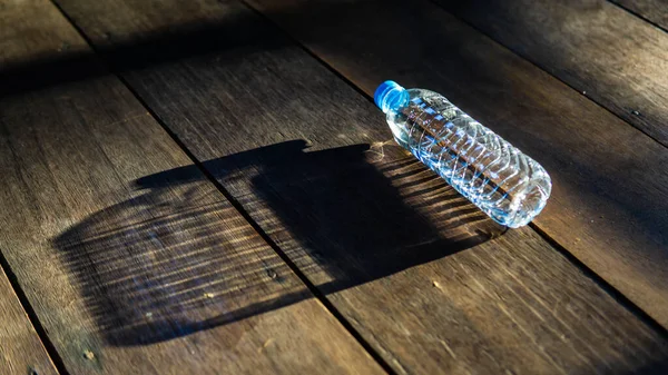 Sunlight rays from outside reflected onto small plastic bottle on the wooden floor and formed a big bottle shadow. Inspirational and hidden opportunities concept. Small outer self, big inner self.