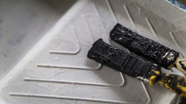 Plastik beyaz boya tepsisinde siyah boya renginde iki kurutulmuş boya fırçası. Seçici açı ve odaklanma. Sanat konsepti.