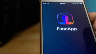 Sungai Buloh, Malaysia - July 20, 2019: An Android user holding a smartphone open up FaceApp application with logo on screen. Apps that edit highly realistic transformations of faces in photographs. clipart