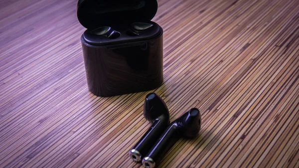 Close up view of black wireless bluetooth earphones or headphones and black box for storage and charging on wooden table background.