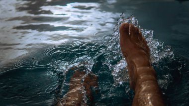 Oteldeki yüzme havuzundan su sıçratarak eğlenen bir adam yaz boyunca gün ışığıyla parlayan bir adam. Karanlık ve kasvetli bir konsept. Seçici görünüm.