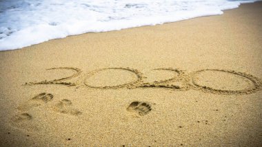 2020 yılınız kutlu olsun. Sahilde deniz dalgalarıyla yazı yazıyoruz. Deniz kıyısında 2020 yıl, kumsalda el yazısıyla yazılmış güzel plaj arkaplanı. Görüntü biraz bulanık. Kumlu ayak izleri.