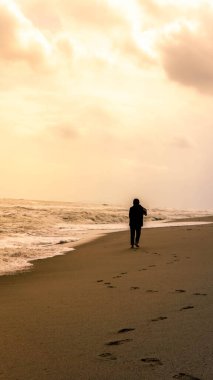 Altın saat boyunca Kuala Terengganu 'daki Batu Burok Sahili' nde tek başına yürüyen tesettürlü bir kızın silueti. Özgürlük kavramı. Rüzgarlı ve büyük deniz dalgaları.
