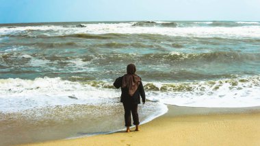 Yazın tropik Batu Burok Sahili 'nde yürüyüş yapan tesettürlü Malezyalı bir kızın manzarası. Görüntü biraz bulanık.