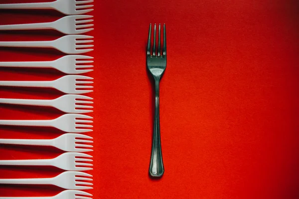 A lot of plastic forks and one metal on a red background. — Stock Photo, Image