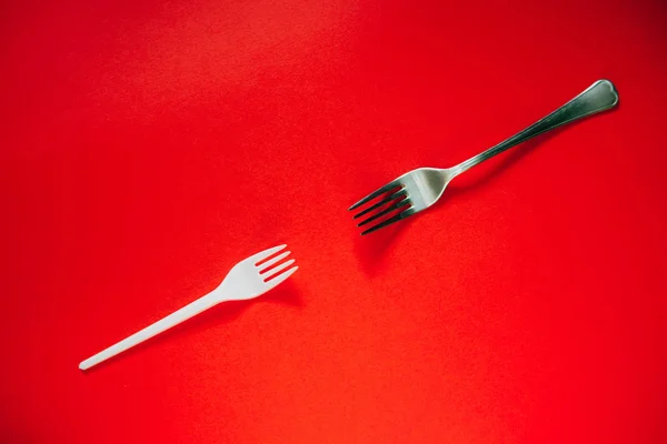 A plastic fork and a metal one on a red background.