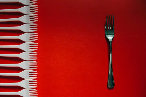 A lot of plastic forks and one metal on a red background. — Stock Photo, Image