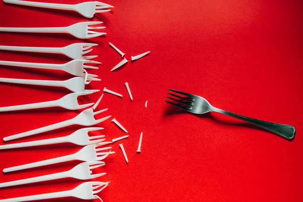 A lot of plastic forks and one metal on a red background.