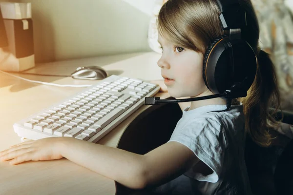 Kafasında kulaklıkla bilgisayarın başında oturan küçük kız.. — Stok fotoğraf