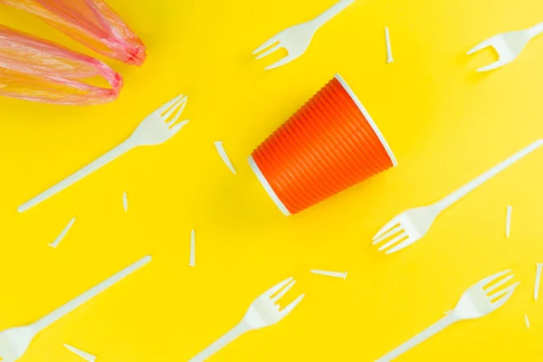 Pattern of broken plastic forks, plastic cup and bag on a yellow background.